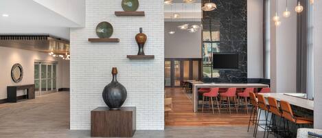A spacious lobby with a high ceiling, a central staircase, and a modern bar area with red chairs.