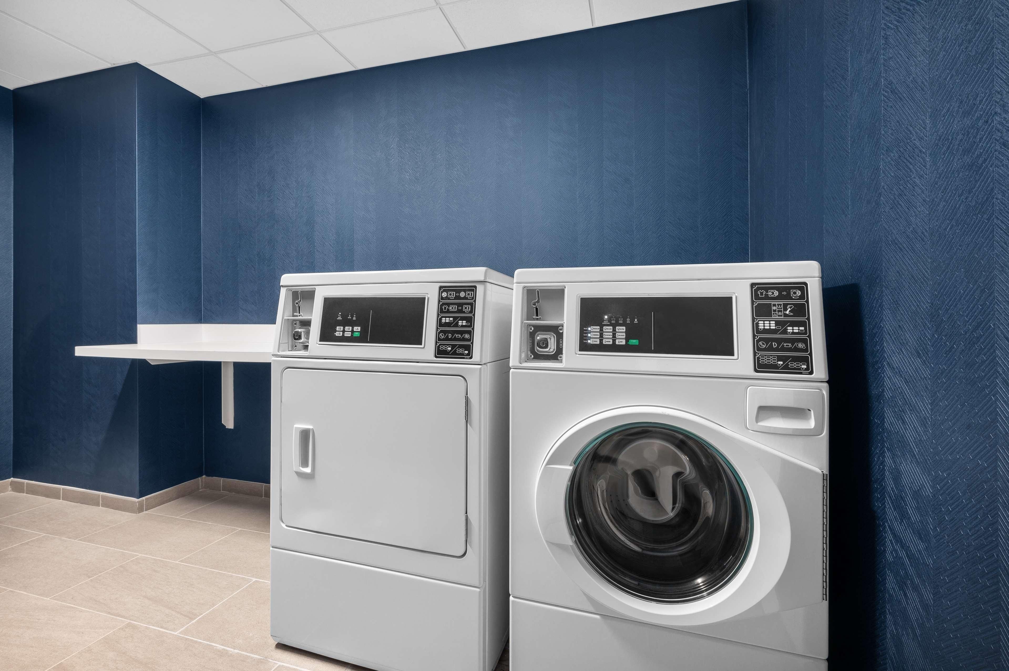 A laundry room with two front-loading washing machines and a white shelf.