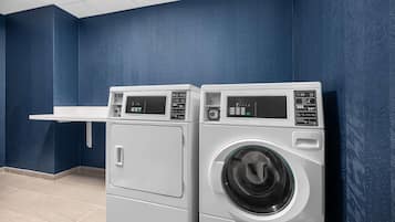 A laundry room with two front-loading washing machines and a white shelf.