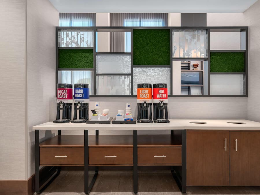 A modern kitchenette with a white countertop, two coffee machines, and a built-in TV.