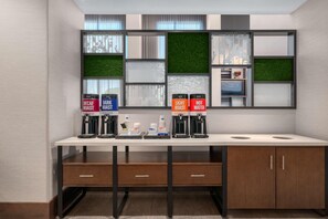 A modern kitchenette with a white countertop, two coffee machines, and a built-in TV. - Hampton Inn & Suites By Hilton Pittsboro (Pittsboro)