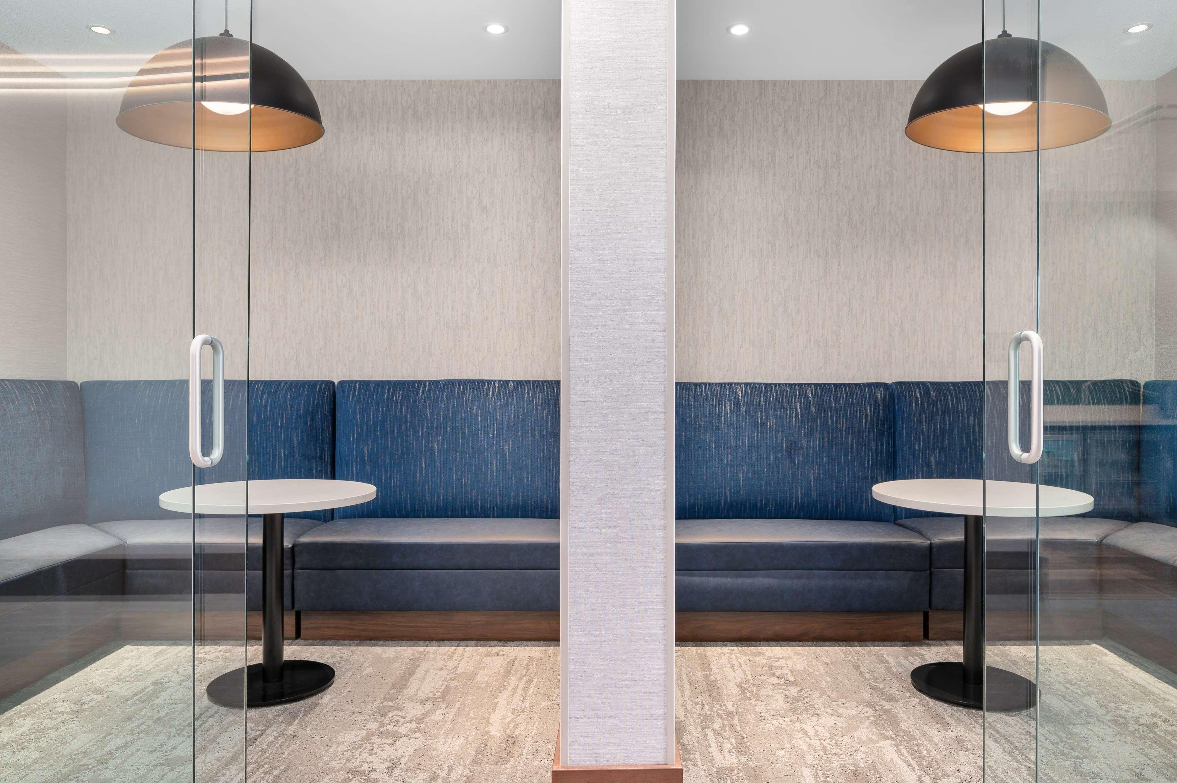 A modern lounge area with a glass partition, two round tables, and a blue sofa.