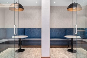 A modern lounge area with a glass partition, two round tables, and a blue sofa.