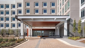 A modern building with a covered entrance, large windows, and a welcoming sign. - Hampton Inn & Suites By Hilton Pittsboro (Pittsboro)