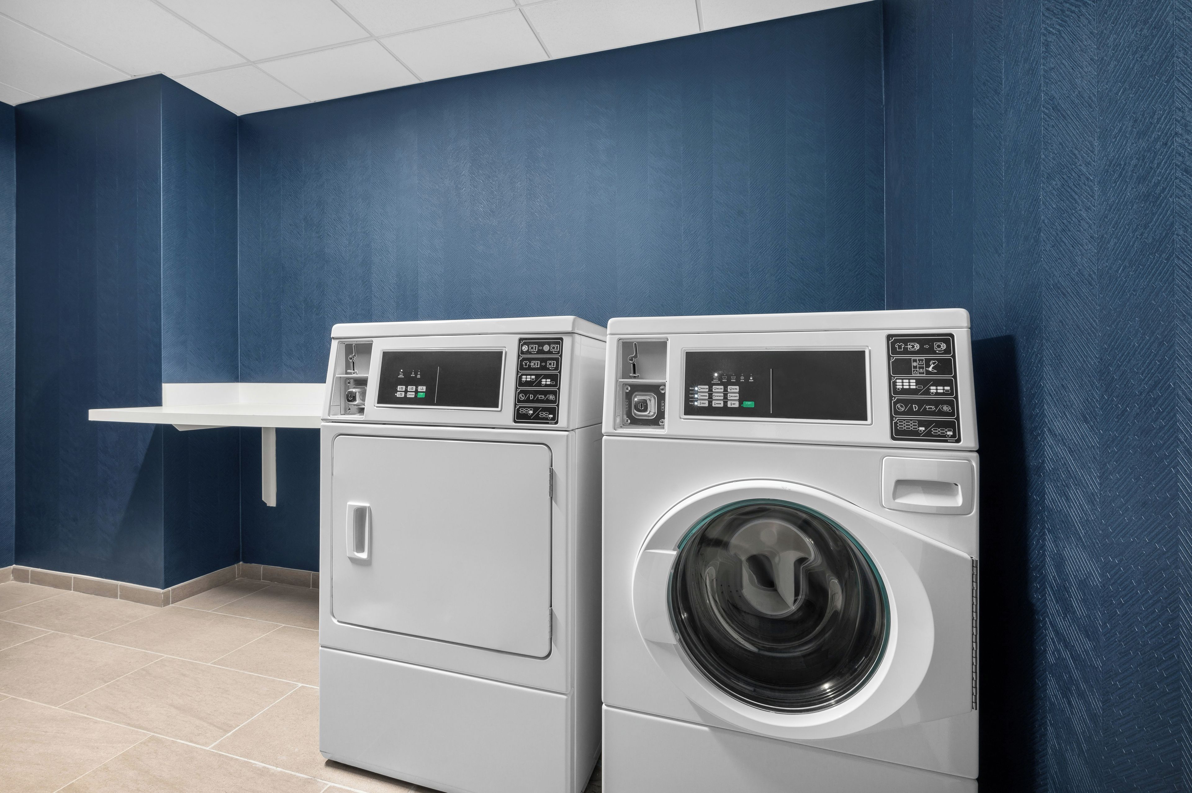 A laundry room with two front-loading washing machines and a white shelf.