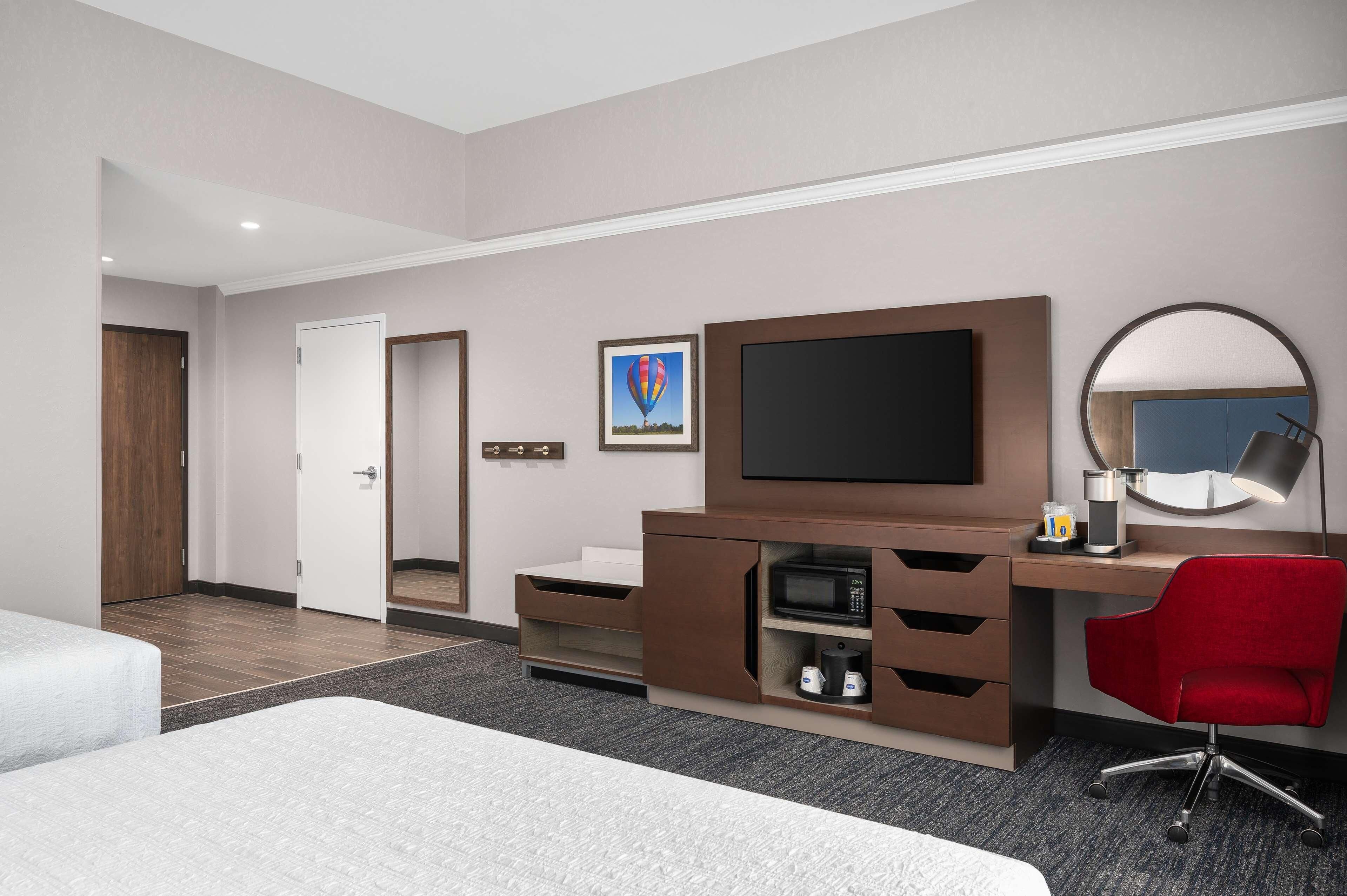 A hotel room with a bed, a desk with a computer, a TV, a microwave, and a red chair.