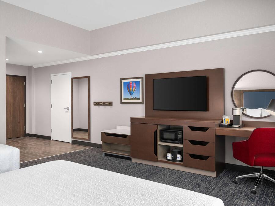 A hotel room with a bed, a desk with a computer, a TV, a microwave, and a red chair.