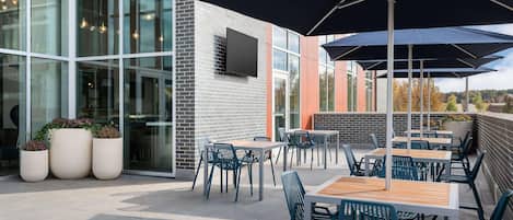 An outdoor patio area with tables and chairs, large umbrellas, and potted plants.