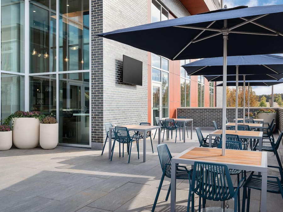 An outdoor patio area with tables and chairs, large umbrellas, and potted plants.