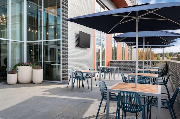 An outdoor patio area with tables and chairs, large umbrellas, and potted plants. - Hampton Inn & Suites By Hilton Pittsboro (Pittsboro)