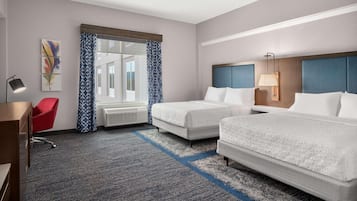 Habitación de hotel con dos camas, un escritorio, una silla y un ventanal con cortinas estampadas.