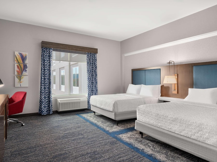 Habitación de hotel con dos camas, un escritorio, una silla y un ventanal con cortinas estampadas.