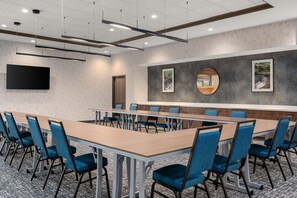 Une salle de conférence avec une longue table, des chaises bleues et un grand écran mural.