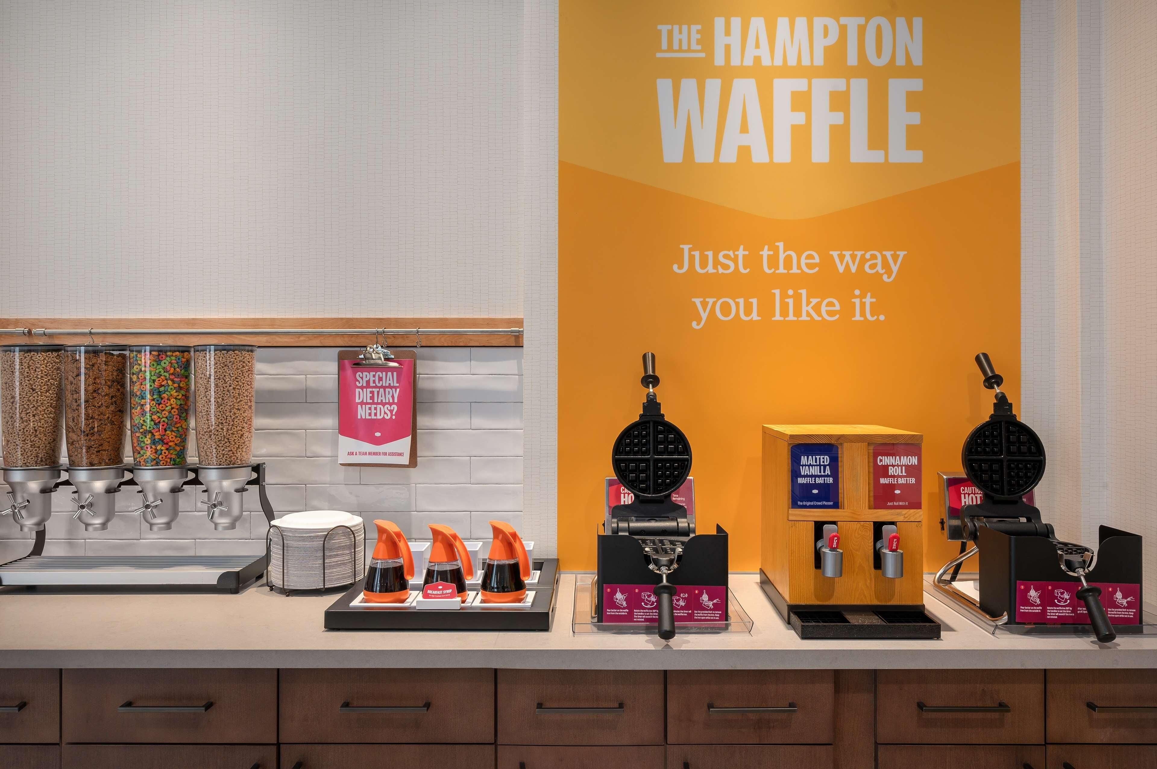 Una cocina con máquinas para hacer gofres, un cartel que dice "The Hampton Waffle" y un cartel preguntando sobre necesidades dietéticas.