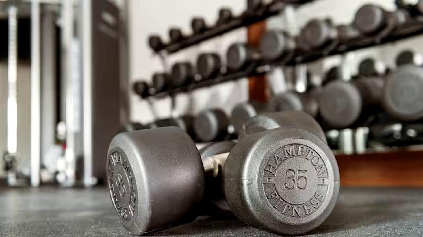 A pair of dumbbells with the brand "HAMPTON FITNESS" and weight "35" lying on a gym floor.