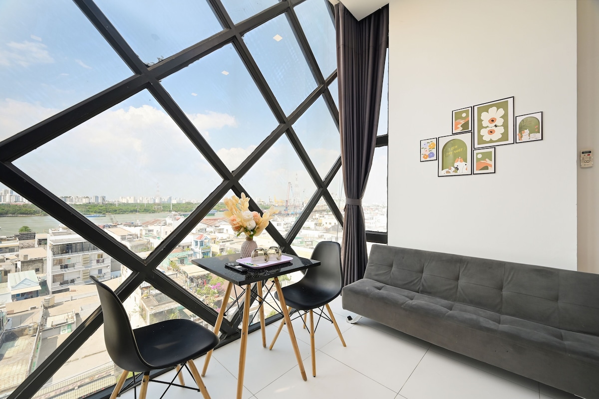 A modern room with a large window, a gray sofa, a small table with chairs, and wall art.