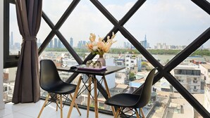 A room with a large window, a table with two chairs, and a vase of flowers. - Huyen Apartment (Ho Chi Minh City)