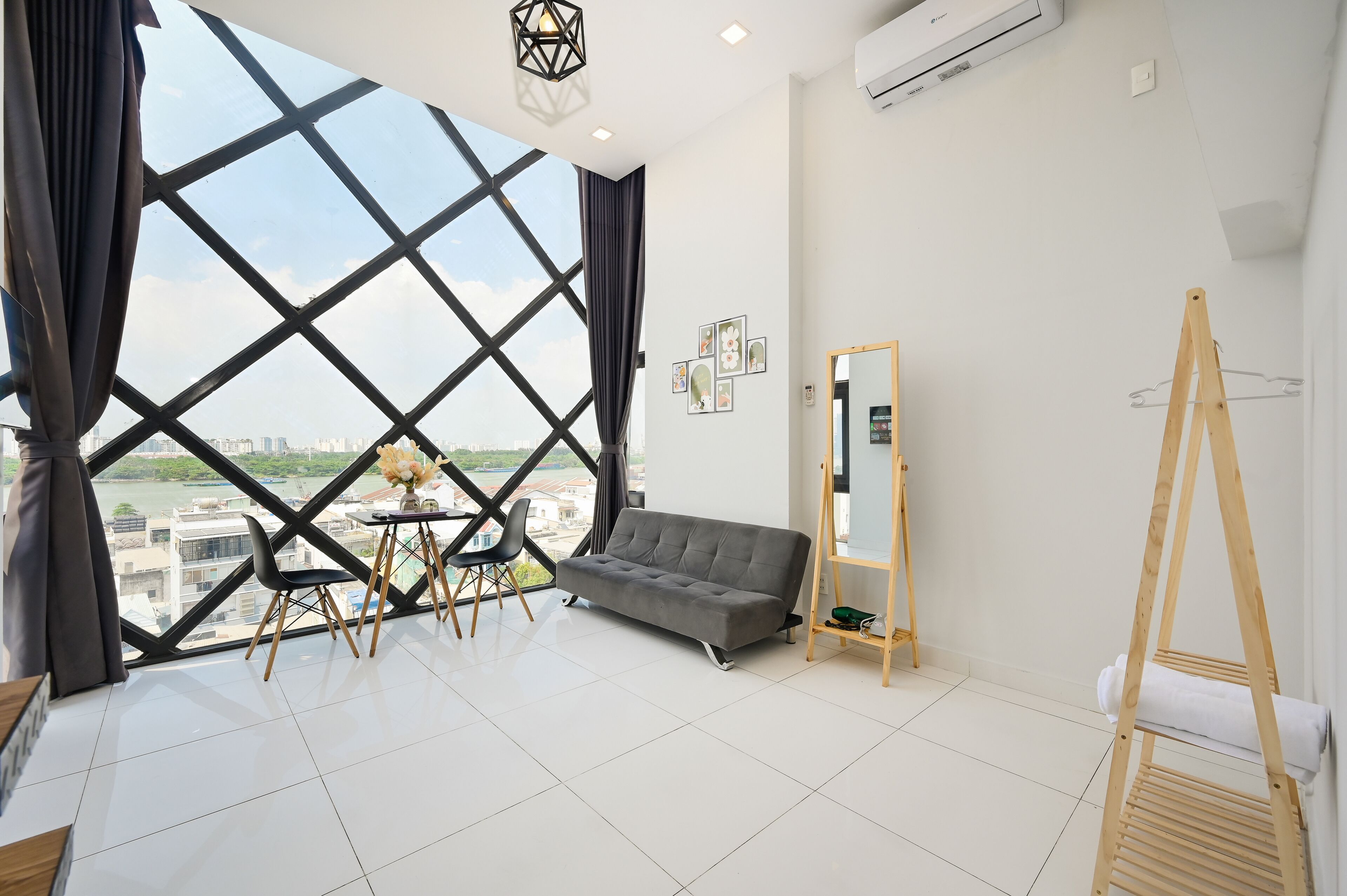 Une pièce moderne avec une grande fenêtre, un canapé gris, un chevalet en bois et une petite table avec des chaises.