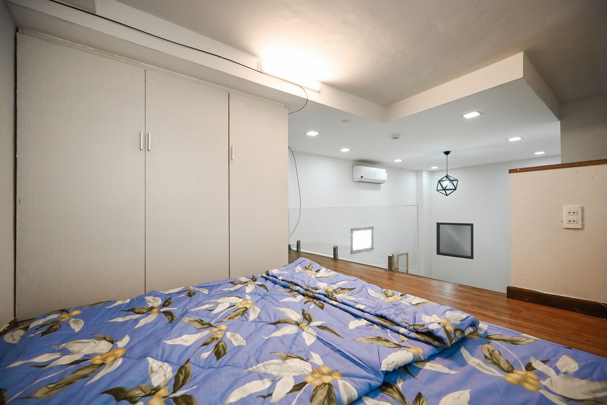 A bedroom with a bed, wardrobe, ceiling lights, and an air conditioning unit.