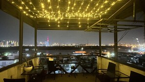 An outdoor seating area with tables and chairs, overlooking a cityscape with a prominent tower. - Huyen Apartment (Ho Chi Minh City)