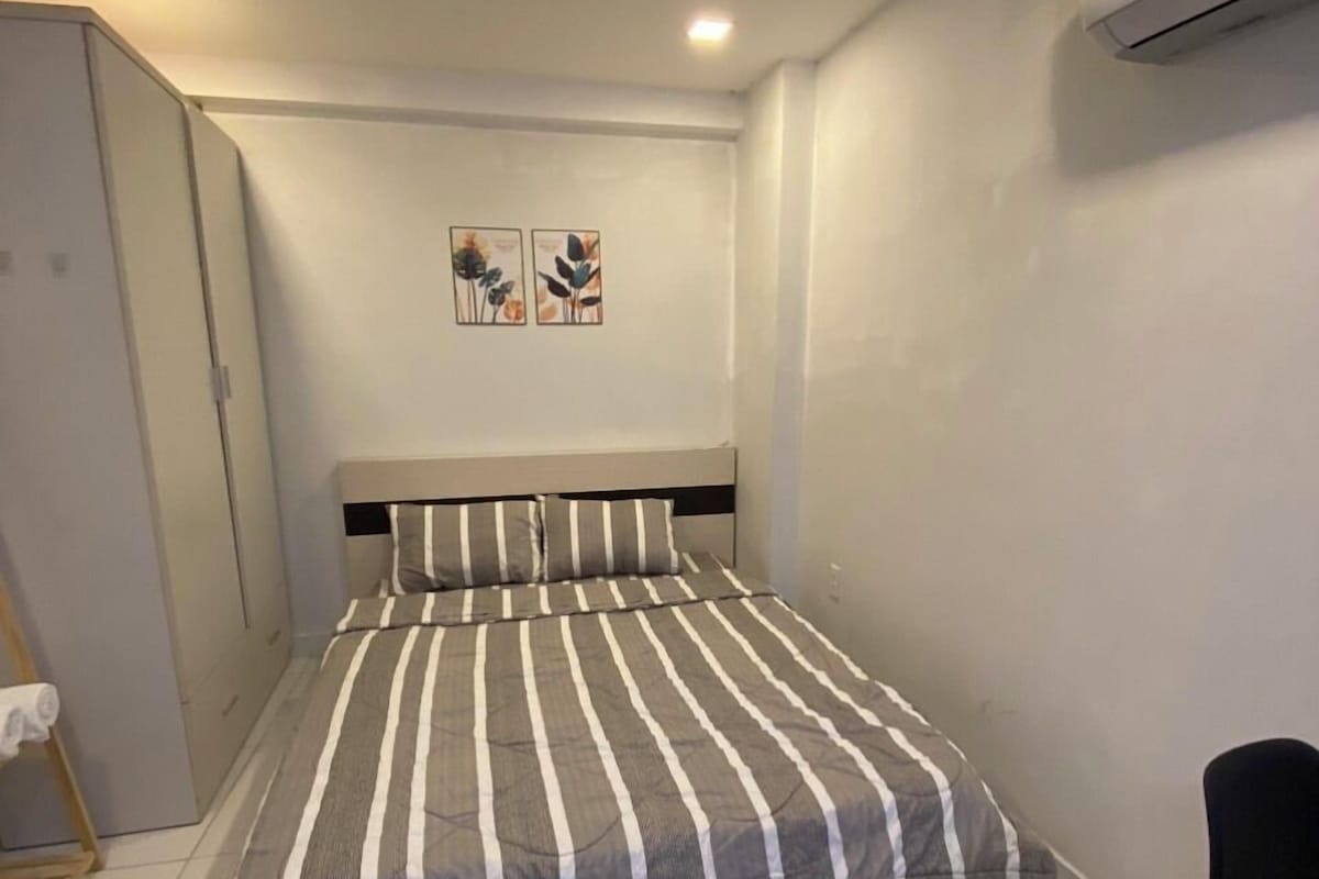 A bedroom with a bed, a chair, an air conditioner, and a wardrobe.