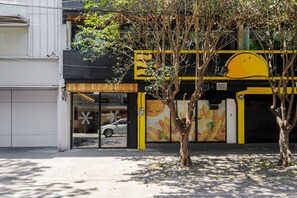 Un bâtiment doté d’une grande fenêtre en verre, d’un arbre devant et d’une enseigne jaune et noire.
