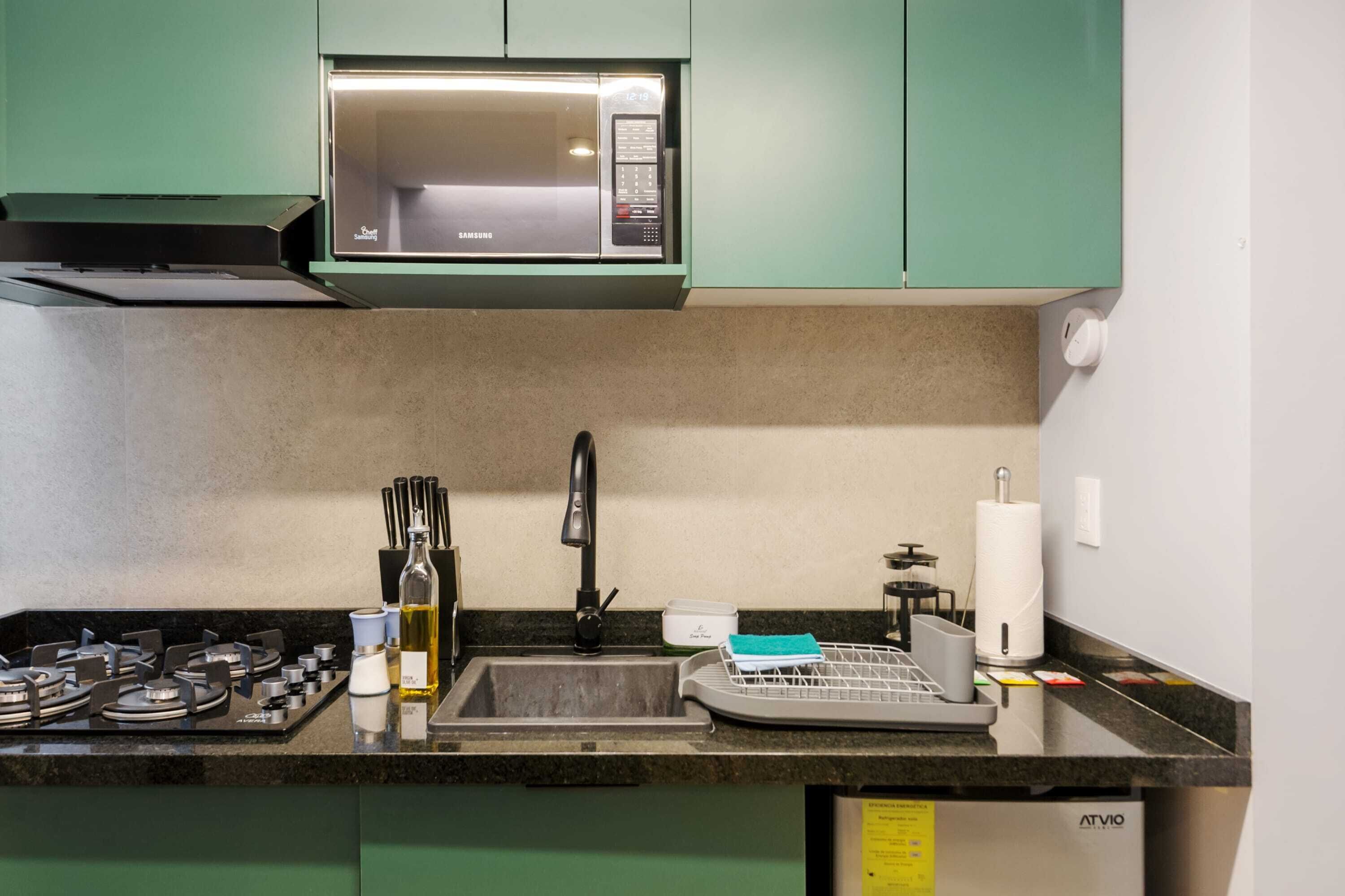 Une cuisine avec des meubles de rangement verts, un four à micro-ondes, une cuisinière à gaz, un évier et un lave-vaisselle.