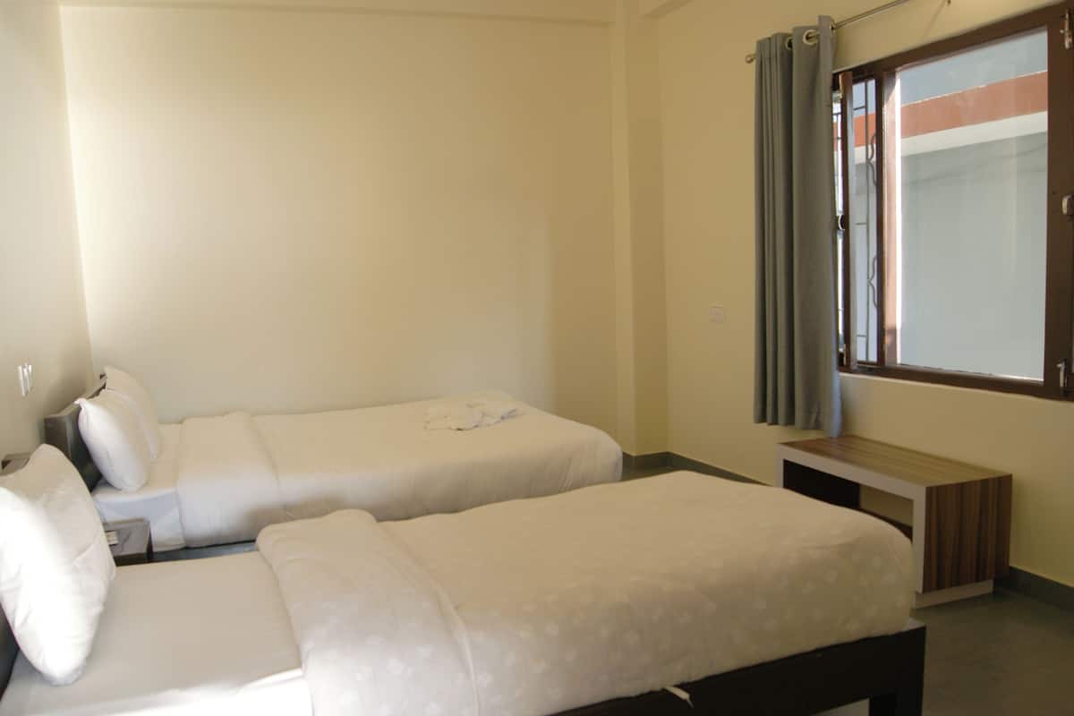 A room with two single beds, a small table, and a window with curtains.