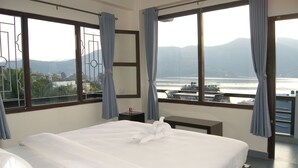 Habitación de hotel con una cama grande, un escritorio y vistas al agua y montañas.