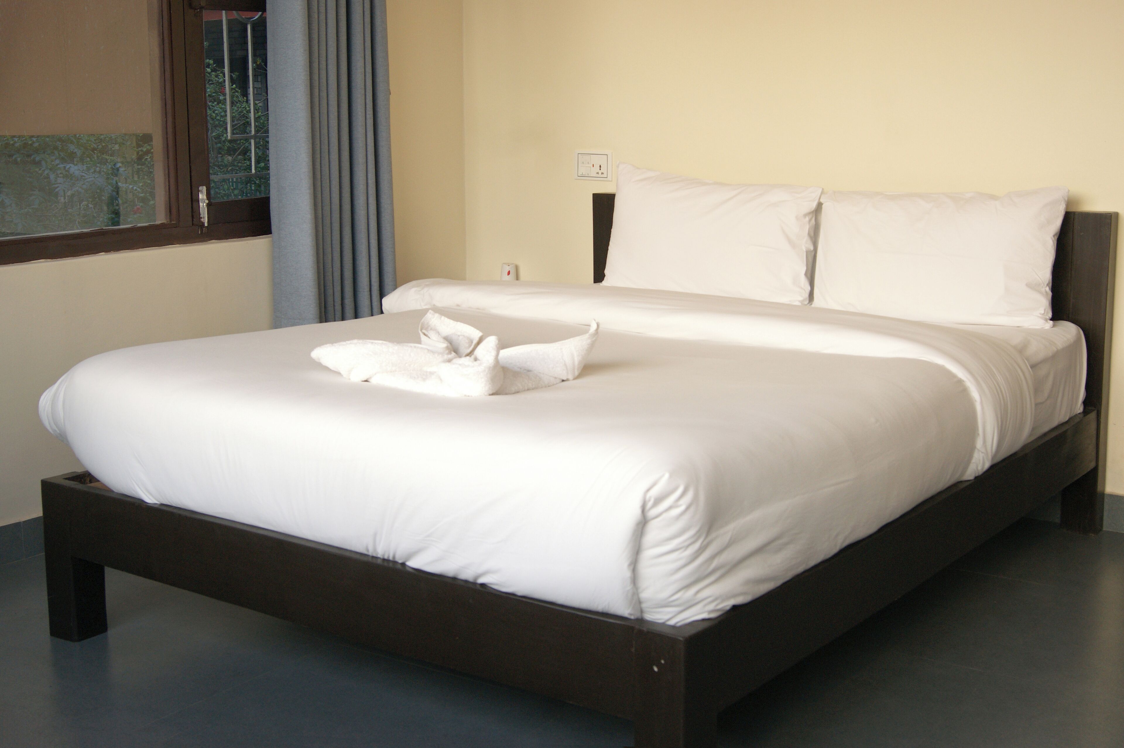 A neatly made bed with white linens and pillows, a dark wooden frame, and a window with curtains.