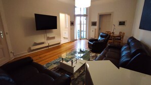 A modern living room with a flat-screen TV, leather sofas, a glass coffee table, and a wooden floor.