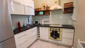 A compact kitchen with white cabinets, a black countertop, a vintage stove, and a small sink.