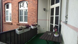 A small balcony with a wooden table, a potted plant, and a window with a white frame.