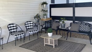 En overdækket terrasse med stole med metalstel, et lille bord og plantekrukker.