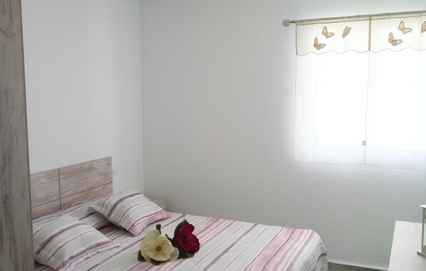 Un dormitorio con cama, almohadas y una ventana con cortina.
