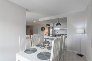 Un comedor moderno con una mesa blanca, individuales grises y una araña.