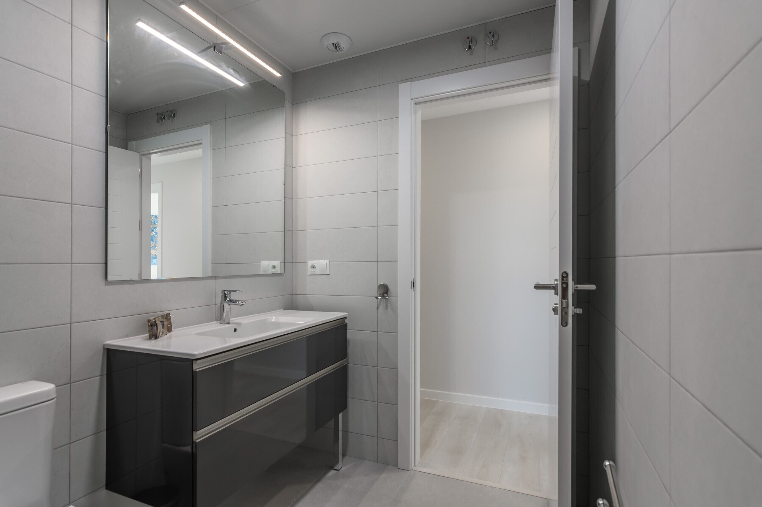 A modern bathroom with a white sink, dark cabinet, and a mirror.