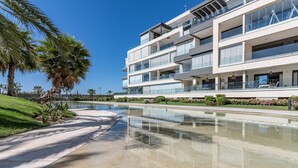 A modern multi-story building with balconies, a reflective pool, and palm trees.