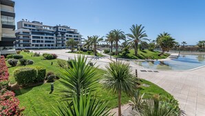 A modern hotel with a pool, palm trees, and a clear blue sky.