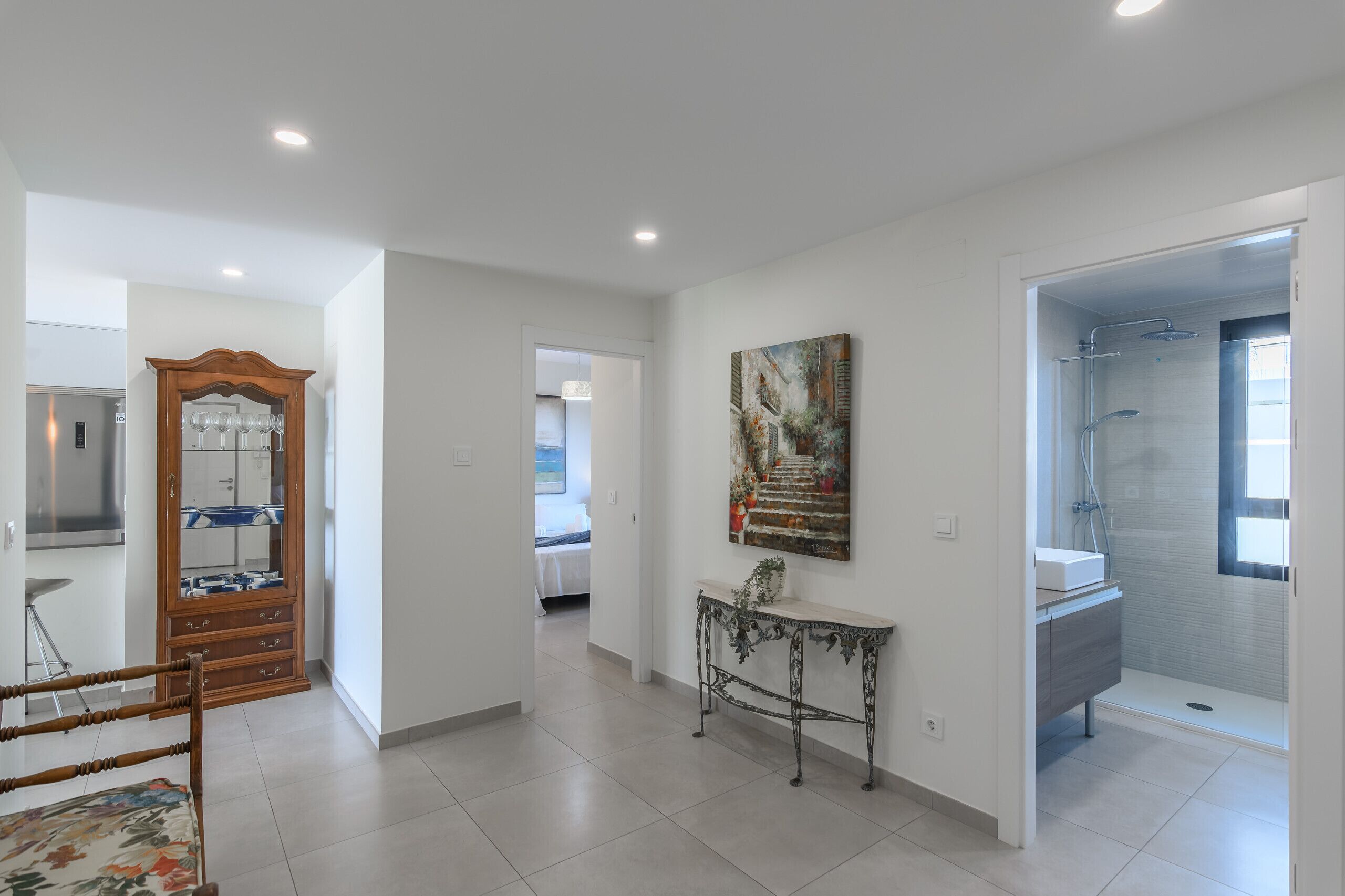 A spacious hallway with a wooden cabinet, a console table, and a painting on the wall.