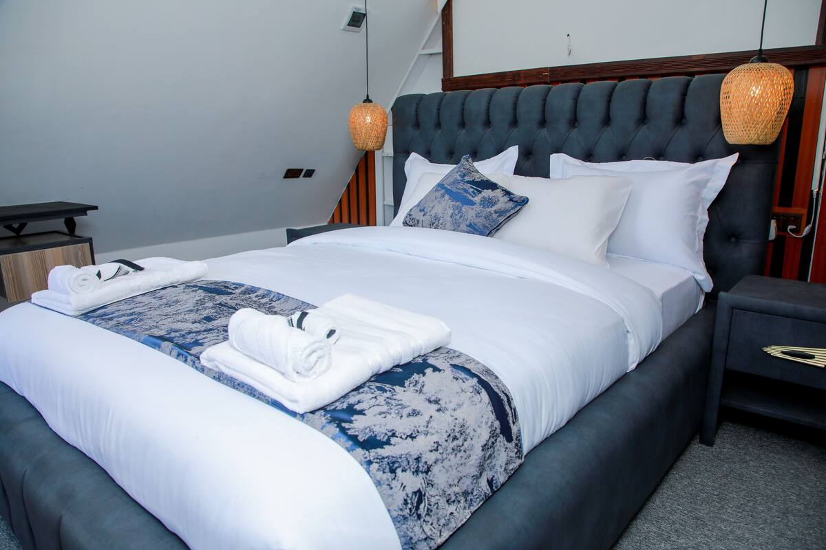 A neatly made bed with white and blue bedding, a dark headboard, and two bedside lamps.
