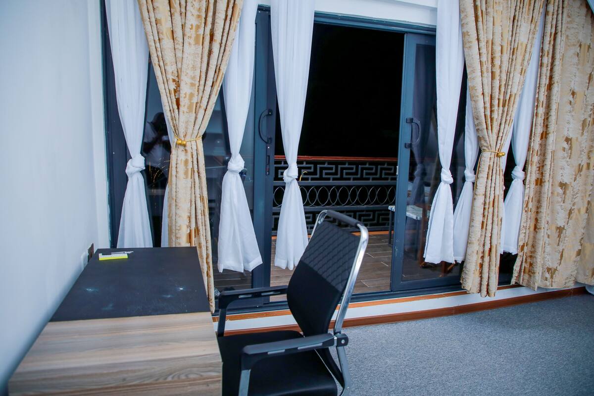 A room with a black chair, a wooden table, and a sliding glass door with patterned curtains.