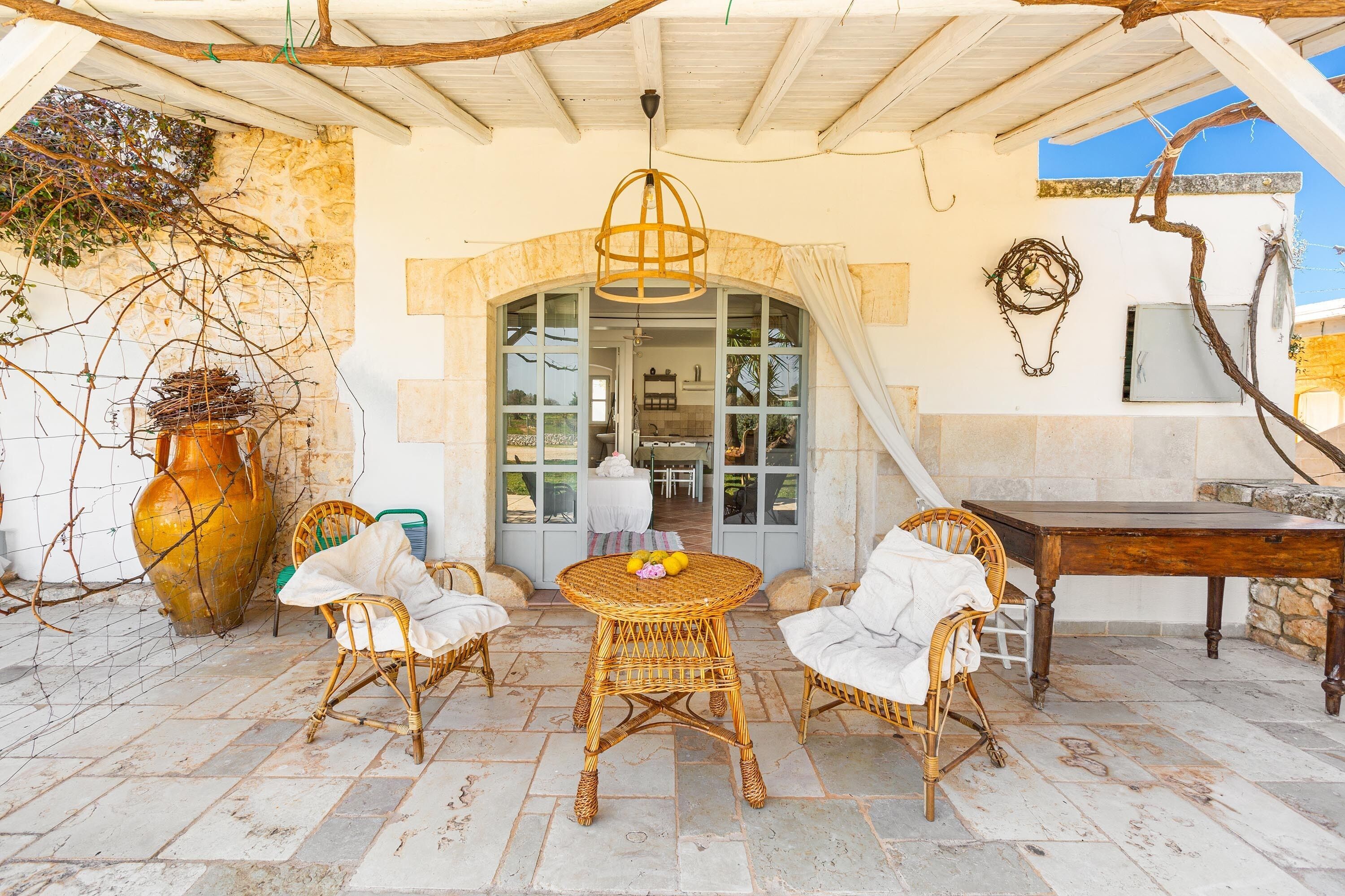 An outdoor patio with wicker furniture, a large vase, and a rustic ceiling.