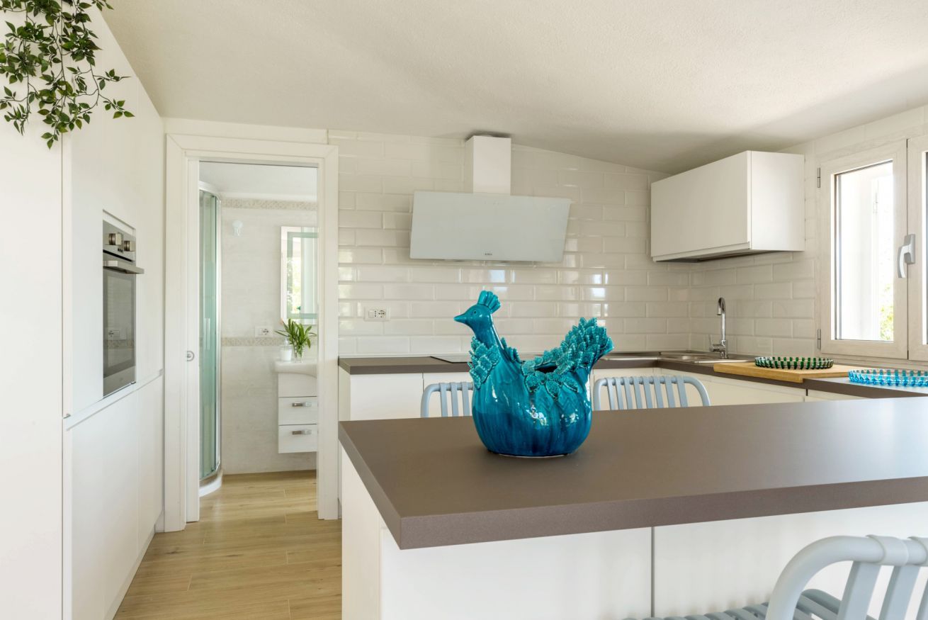 A modern kitchen with white cabinets, a central island, and a blue decorative vase.