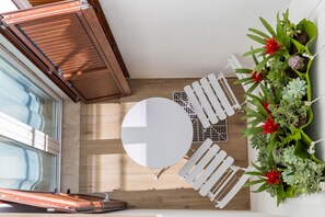 Ein kleiner, offener Wohnbereich mit rundem Tisch und weißen Stühlen, Holzboden und einer grünen Wand aus Pflanzen.