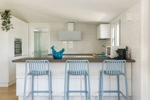 Una cocina moderna con armarios blancos, una isla central con taburetes de bar y un jarrón azul decorativo.