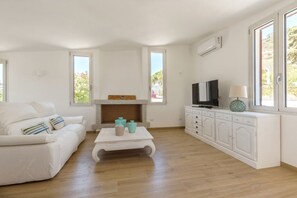 Ein geräumiges Wohnzimmer mit einem weißen Sofa, einem Couchtisch mit Dekoration, einem Kamin, einem Fernseher und einem Schrank.