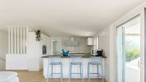 Una cocina moderna con una isla central, tres taburetes de bar y un amplio ventanal corredera a la derecha.