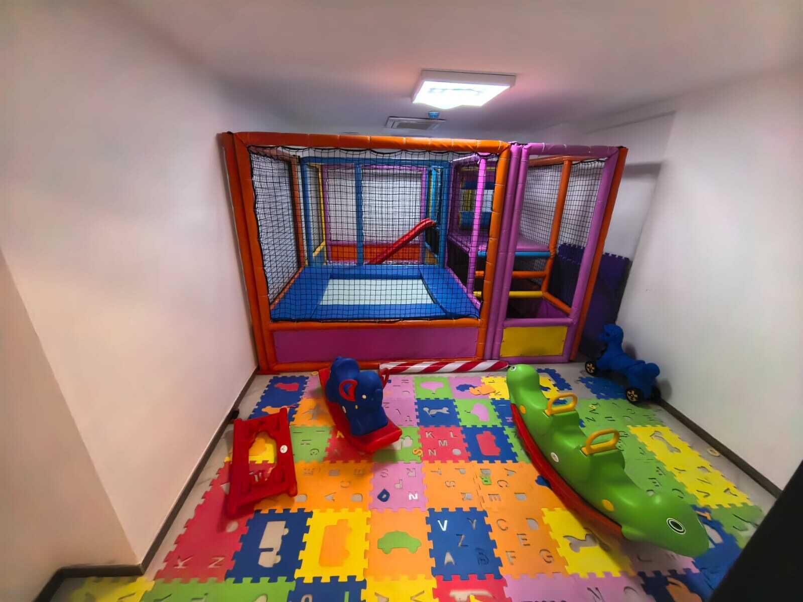 Zona de juegos con suelo acolchado, estructura de juego con red y coloridos tapetes de espuma.