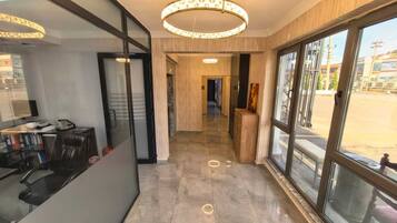 Vestíbulo de hotel con diseño moderno, que incluye un mostrador de recepción, una lámpara de araña grande y vistas a través de puertas de cristal.